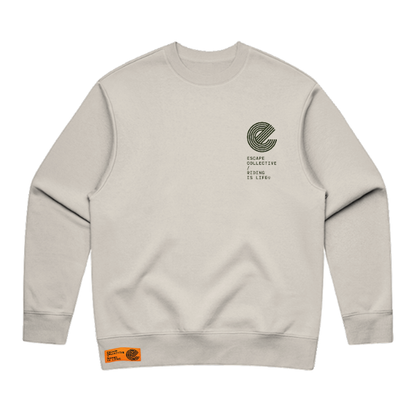 A light beige crewneck sweatshirt with a dark green circular graphic and text on the left chest, featuring a small orange brand patch on the bottom hem.